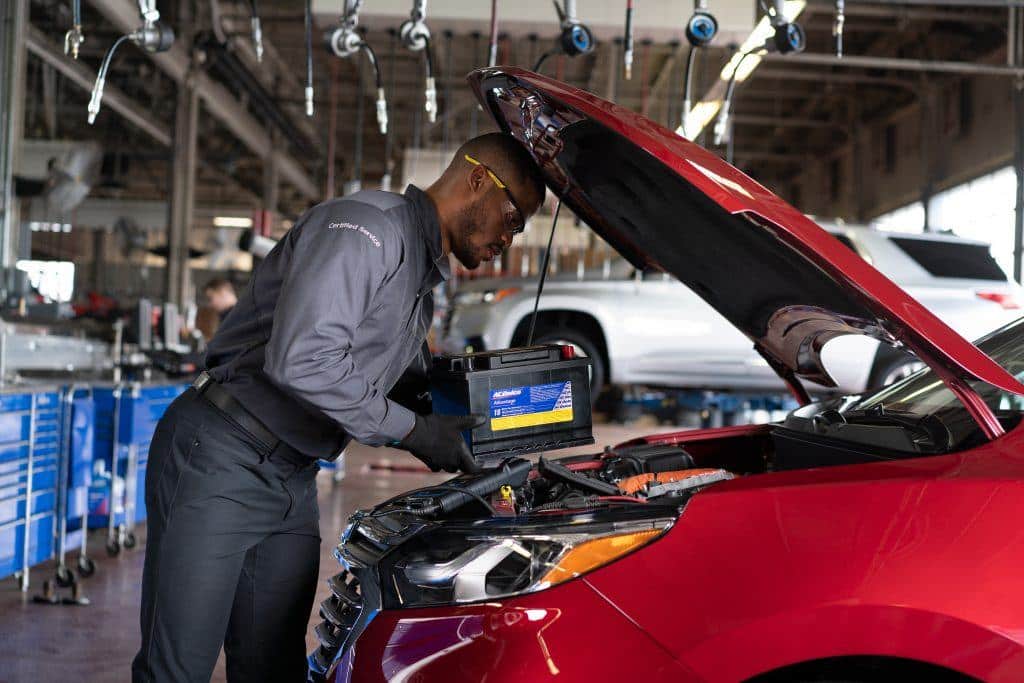 Mechanic replacing car battery in a red vehicle at an auto repair shop.