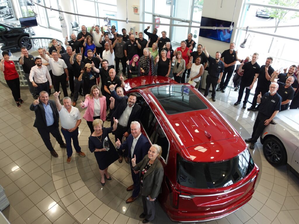 Group of people celebrating around a red car in a showroom, highlighting teamwork and automotive success.