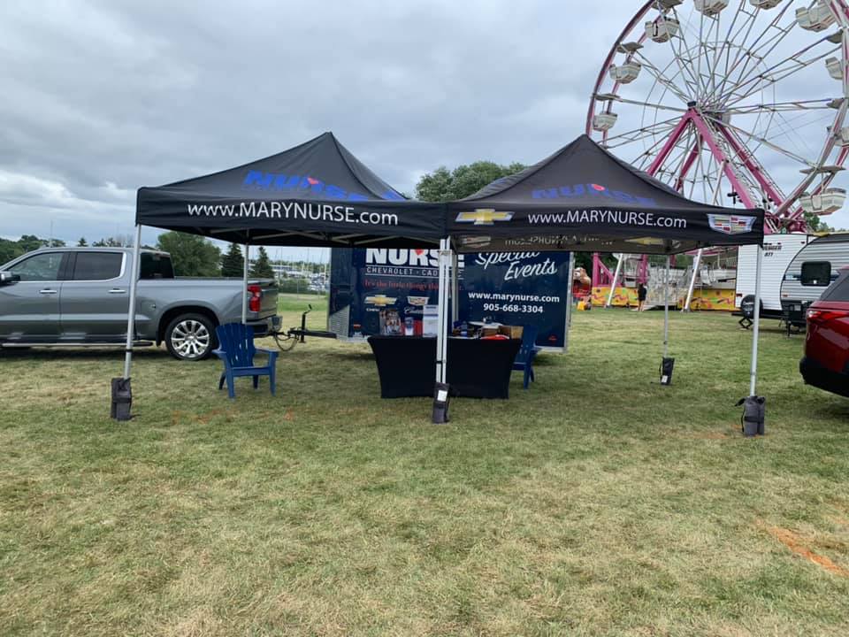 Outdoor event booth with Mary Nurse Chevrolet-Cadillac branding near a Ferris wheel.