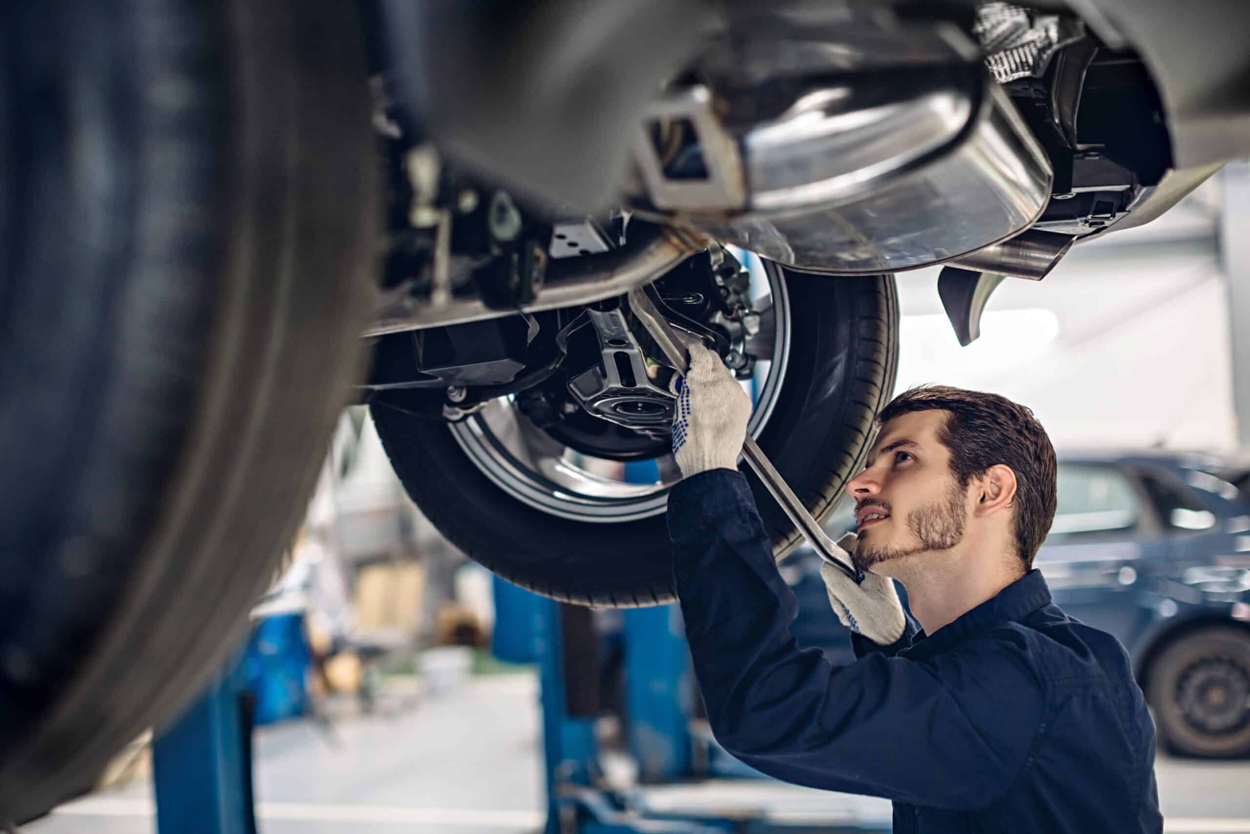 Mechanic using wrench to repair car undercarriage in auto repair shop.
