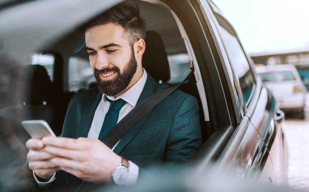 Man in a suit smiling while using a smartphone in a car, conveying business and connectivity.