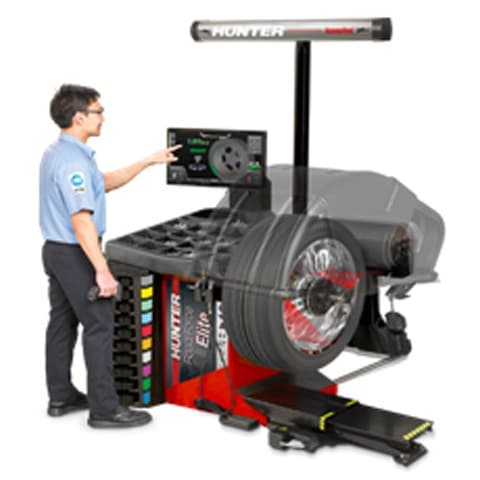 Technician operates Hunter wheel balancer, showcasing tire alignment technology.
