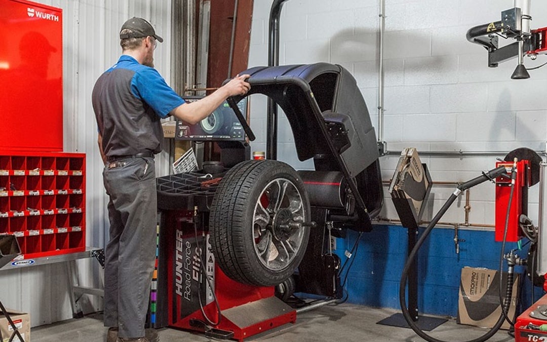 Mechanic tightening a wheel on a lifted SUV with a power tool in an auto repair shop.