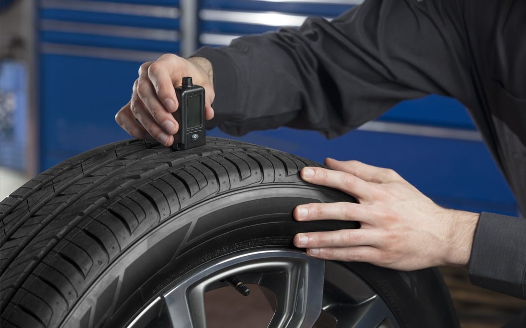 Mechanic tightening a wheel on a lifted SUV with a power tool in an auto repair shop.