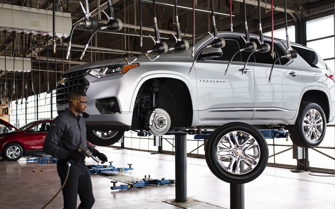 Mechanic tightening a wheel on a lifted SUV with a power tool in an auto repair shop.