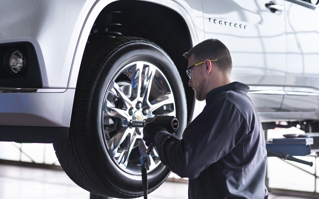 Mechanic tightening a wheel on a lifted SUV with a power tool in an auto repair shop.