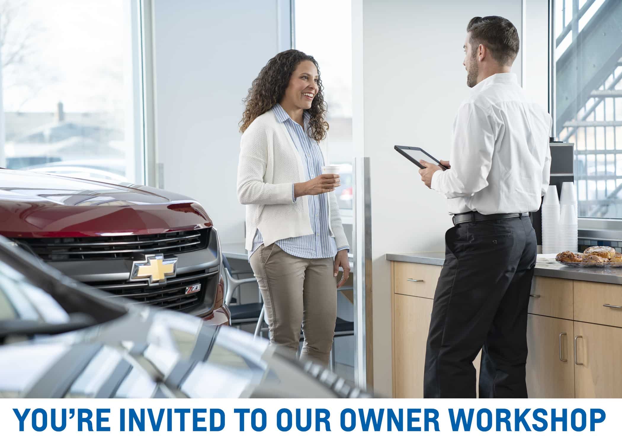 Chevrolet owner workshop invitation, featuring a friendly chat between a woman and a man holding a tablet in a showroom.