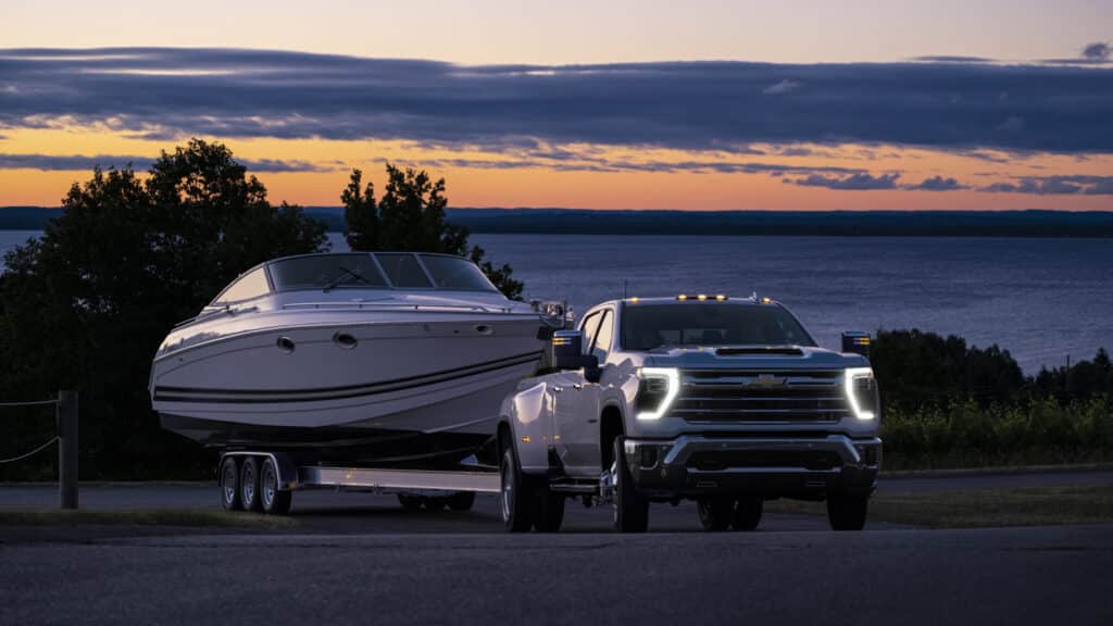 Truck towing a speedboat at sunset by a lake, with silhouetted trees in the background.