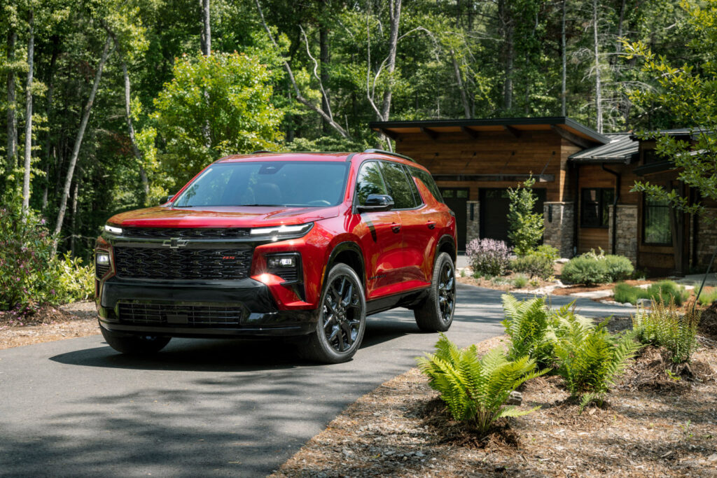 Red SUV parked on a driveway in front of a modern house surrounded by trees and greenery.