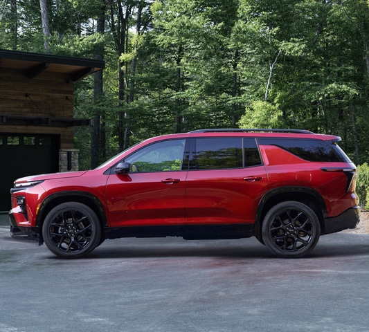 Red SUV parked in front of a modern house, surrounded by lush green forest.