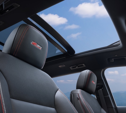Car interior with Z71-embroidered seats and panoramic sunroof showing blue sky and clouds.