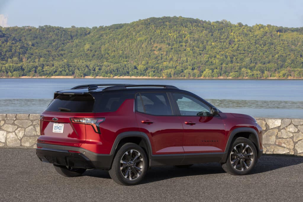 Red SUV parked by a scenic lakeside with lush green hills in the background.