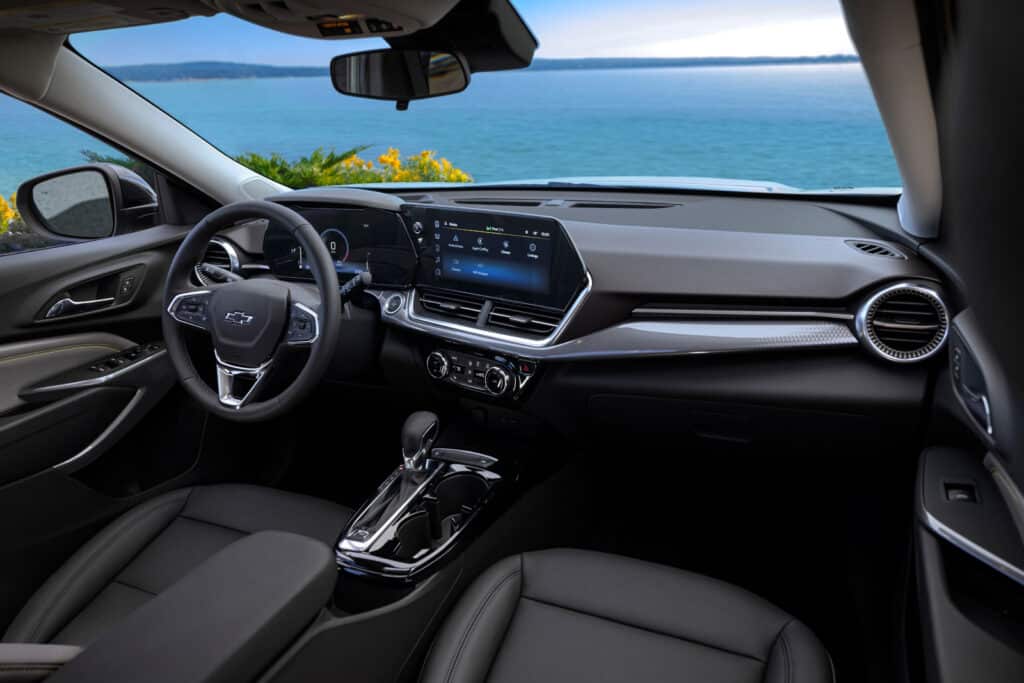 Modern car interior with digital dashboard, sleek steering wheel, and scenic ocean view in the background.