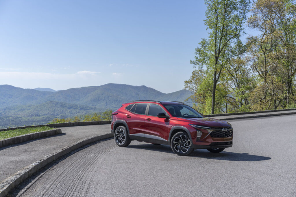Red SUV parked on a scenic mountain road, surrounded by lush green hills and trees under a clear blue sky.