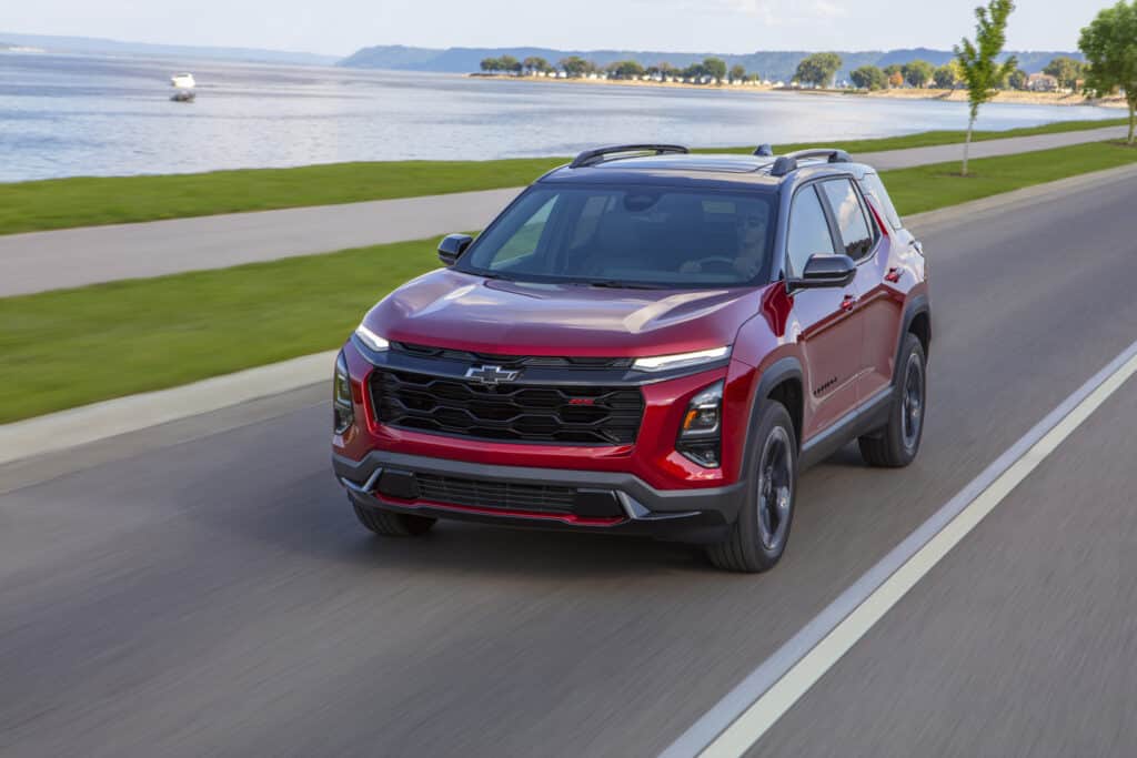 Red Chevrolet SUV driving on a scenic lakeside road, showcasing sleek design and modern features.