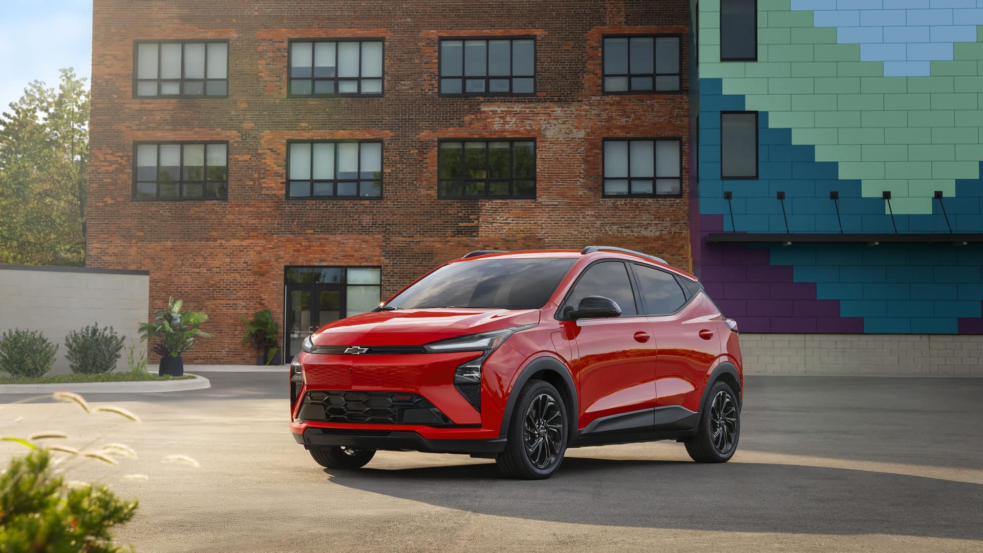 Red Chevrolet SUV parked in front of a brick building and colorful mural wall.