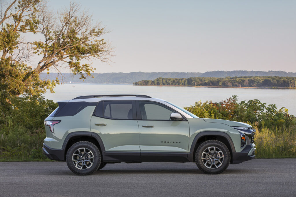 SUV parked by a scenic lakeside with lush greenery and distant hills, under a clear sky.