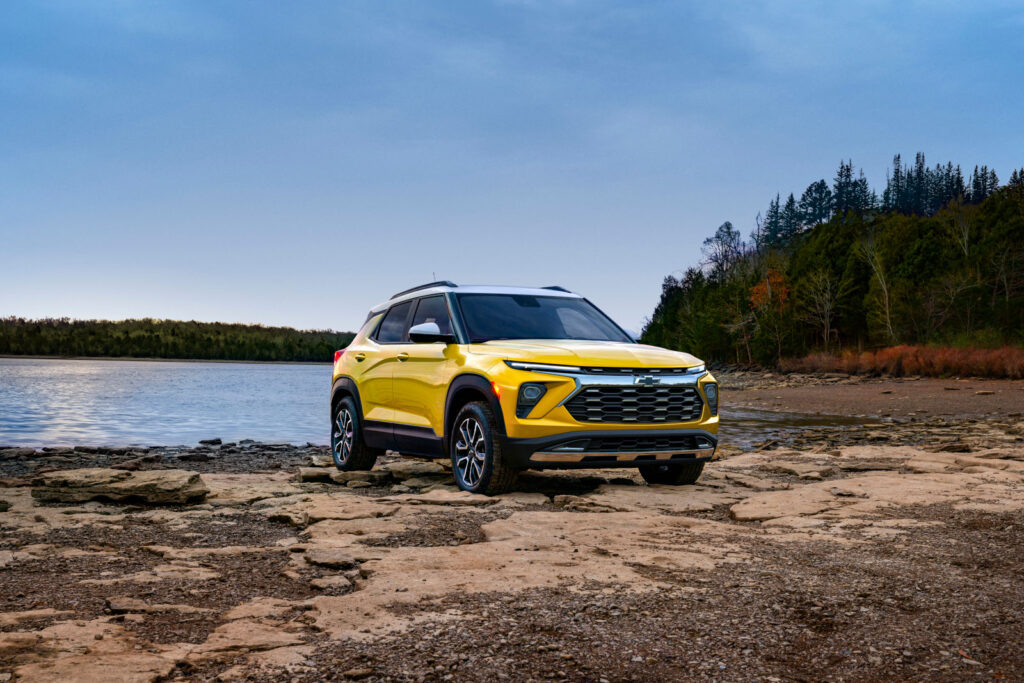 Yellow SUV parked by a lake, surrounded by rocky terrain and forested background.