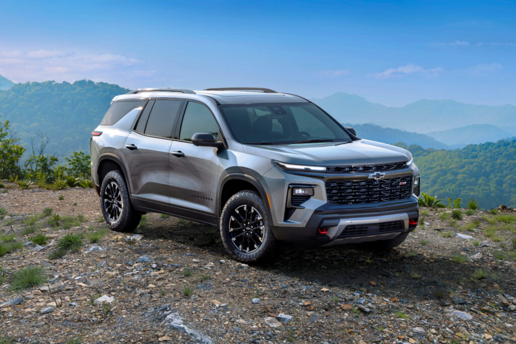 Silver SUV on rocky terrain with a scenic mountain backdrop under a clear blue sky.