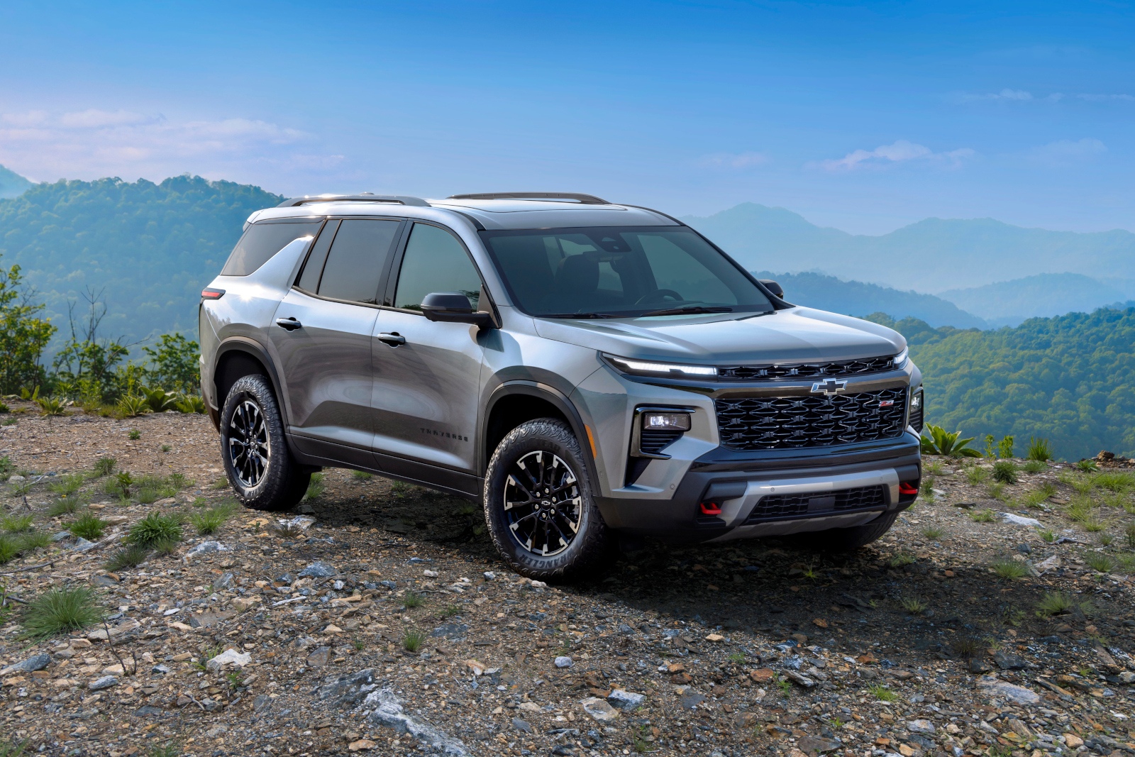 Silver SUV on rocky terrain with a scenic mountain backdrop under a clear blue sky.