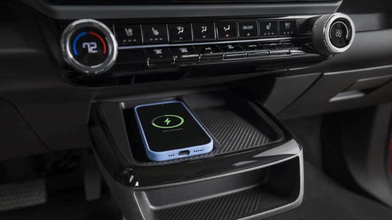 Car interior with a smartphone wirelessly charging below a digital climate control panel.