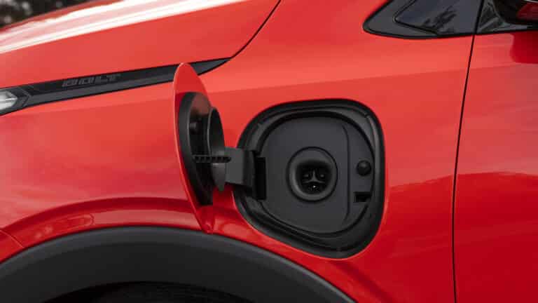 Electric vehicle charging port on a red car's side, open and ready for charging.