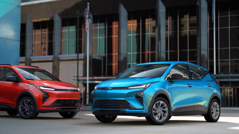 Two modern electric SUVs, one red and one blue, parked in an urban setting with tall buildings.