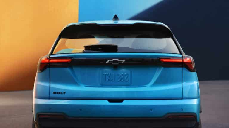 Blue Chevrolet Bolt viewed from the rear with a blurred license plate, set against a colorful backdrop.