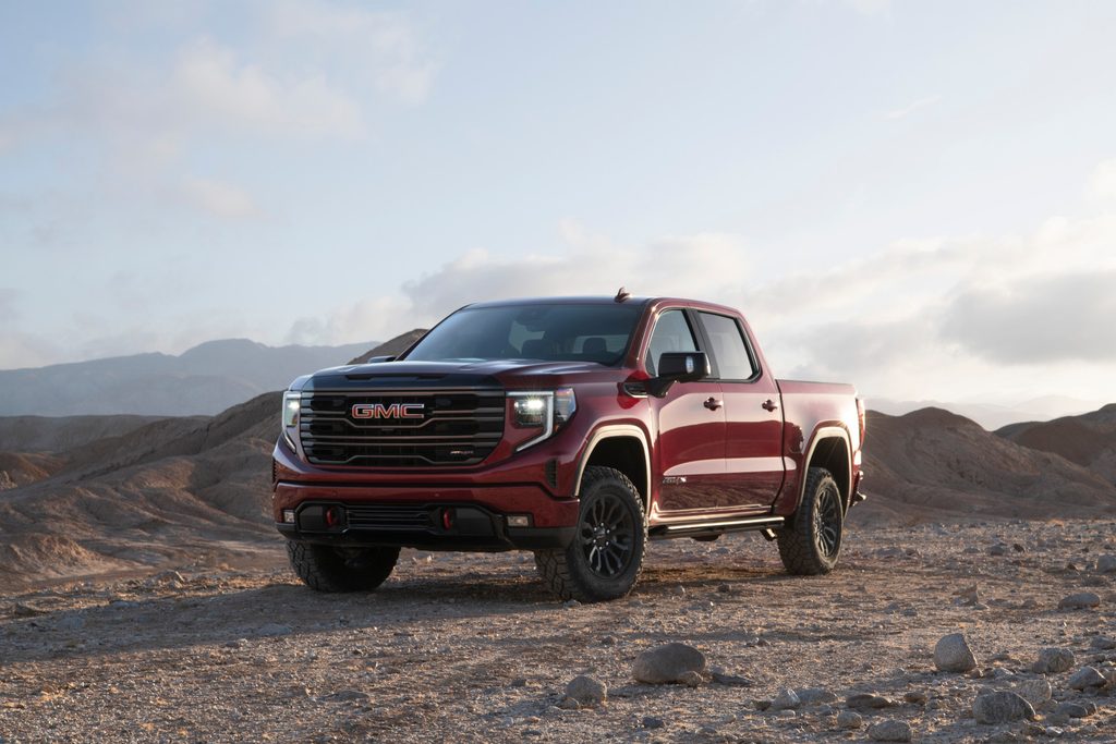 Red GMC pickup truck parked on rugged desert terrain under a partly cloudy sky.