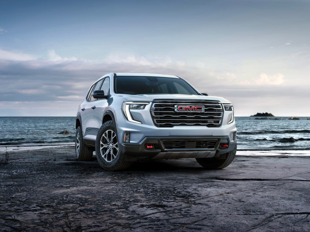 White GMC SUV parked by the ocean on rocky terrain, under a cloudy sky.