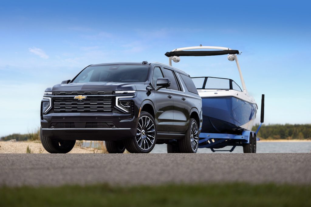 SUV towing a blue boat on a trailer, parked by a lakeside with a clear blue sky.
