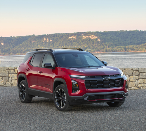 Red SUV parked by a lake with a scenic mountain backdrop under a clear sky.