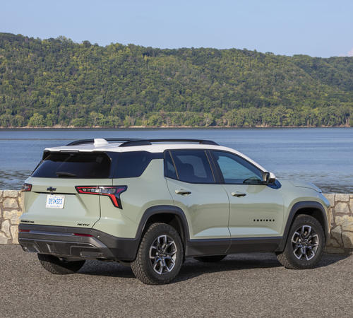 SUV parked by a lakeside with a forested hill in the background on a clear day.