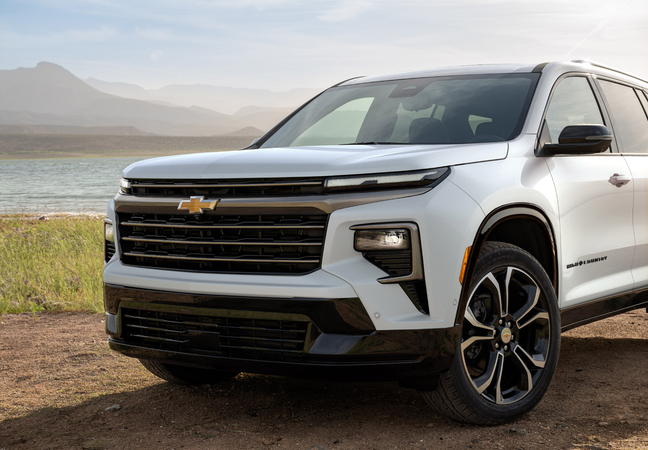 White Chevrolet SUV parked near a lakeside with mountains in the background, under a clear sky.