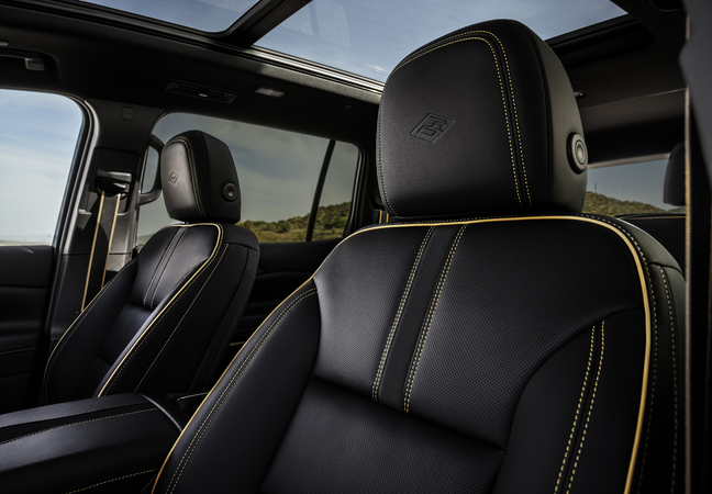 Luxurious car interior featuring black leather seats with yellow stitching, panoramic sunroof view.