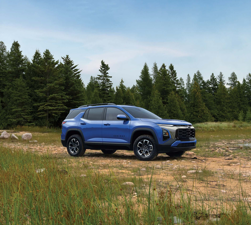 Blue SUV parked on rocky terrain with a background of dense green forest under a clear sky.