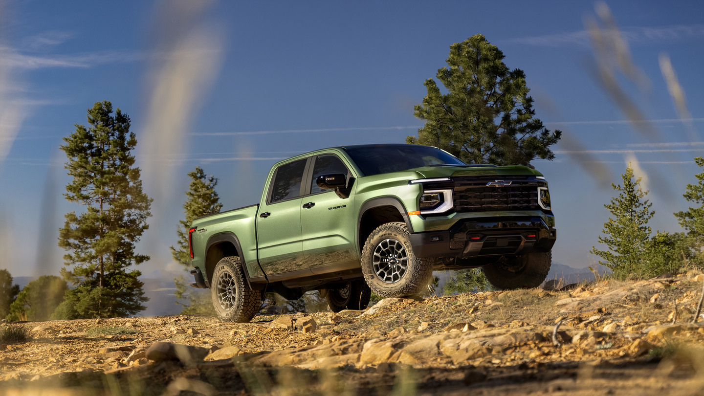 A green Chevrolet Silverado truck displayed in a rugged, scenic outdoor setting with trees and a clear sky.